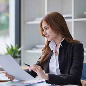 Elegant businesswoman analyzes financial reports at her office desk inside..