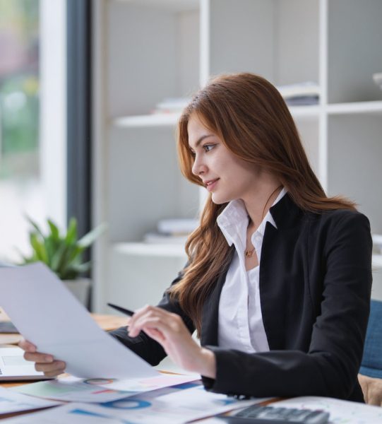 Elegant businesswoman analyzes financial reports at her office desk inside..